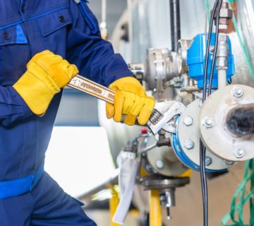 Technician in factory at machine maintenance working with wrench